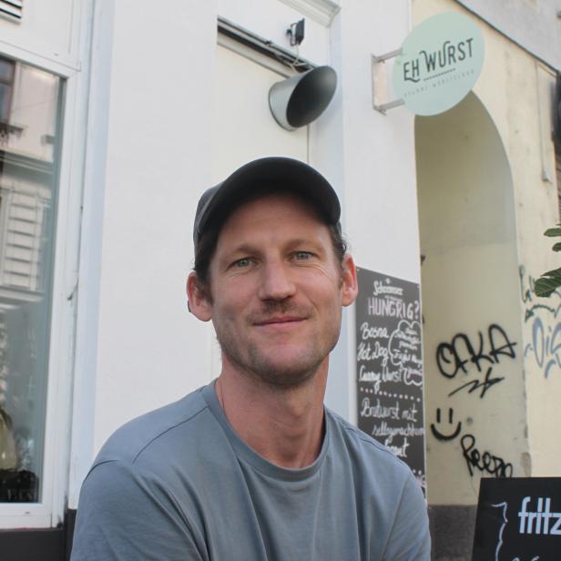 Ein Mann mit Kappe sitzt vor dem Imbiss „EH Wurst“.