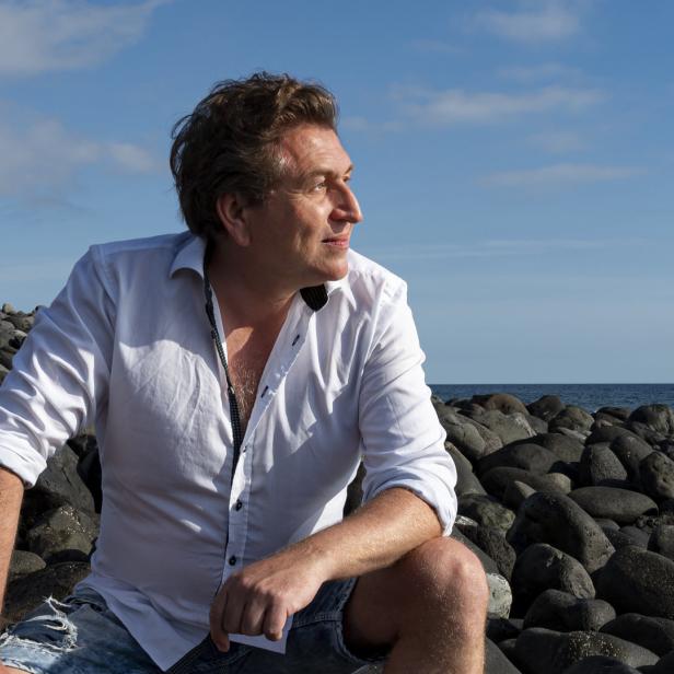 Ein Mann sitzt auf einem Felsenstrand und blickt aufs Meer.
