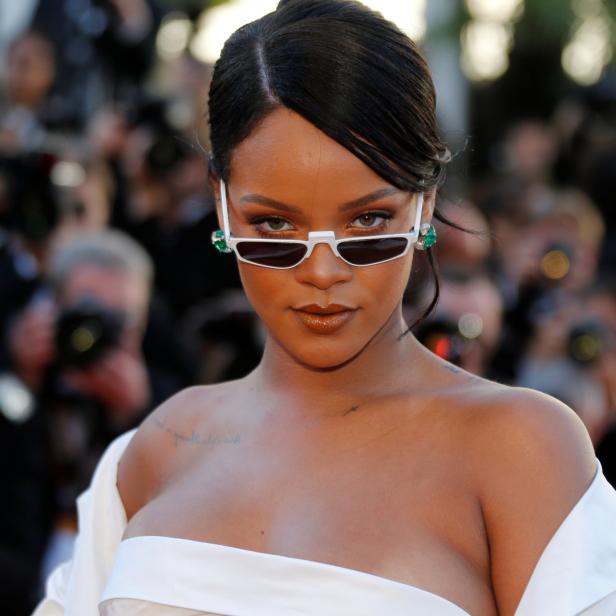 Rihanna posiert mit weißer Sonnenbrille und passendem Oberteil auf dem roten Teppich.