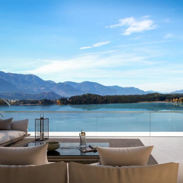 Von einer Terrasse blickt man auf einen See und eine bewaldete Hügellandschaft.