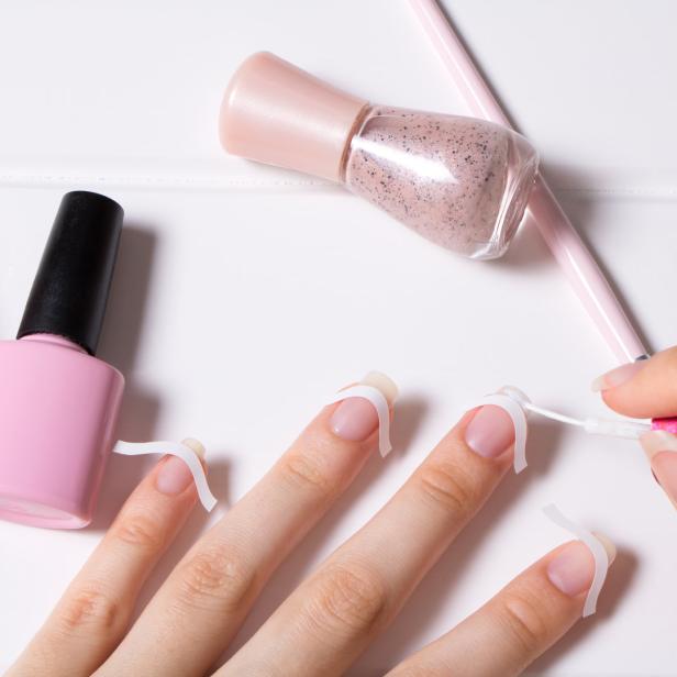 Eine Hand lackiert die Nägel mit rosa Nagellack, während Schablonen verwendet werden.
