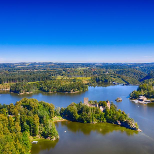 Luftaufnahme der Burgruine Rabenstein auf einer bewaldeten Insel im See Rabenstein bei Chemnitz.