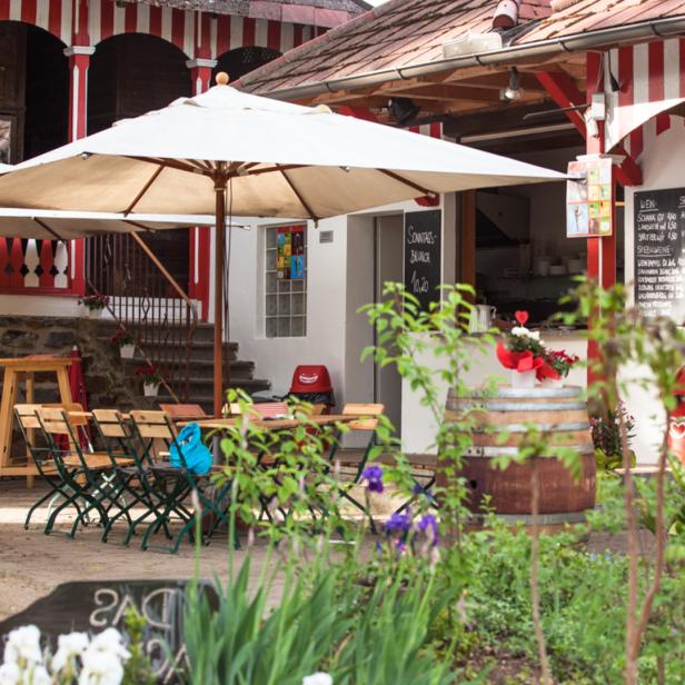 Einladender Außenbereich eines Cafés mit Tischen, Stühlen und Sonnenschirmen.