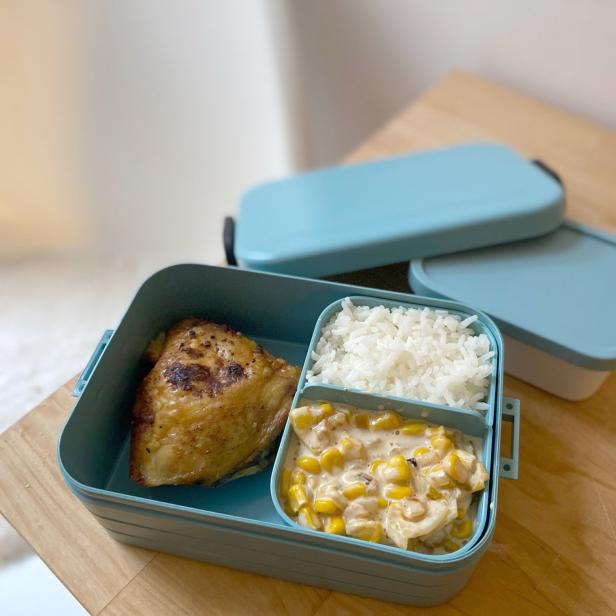 Eine blaue Bento-Box mit Hähnchen, Reis und Maisgemüse.
