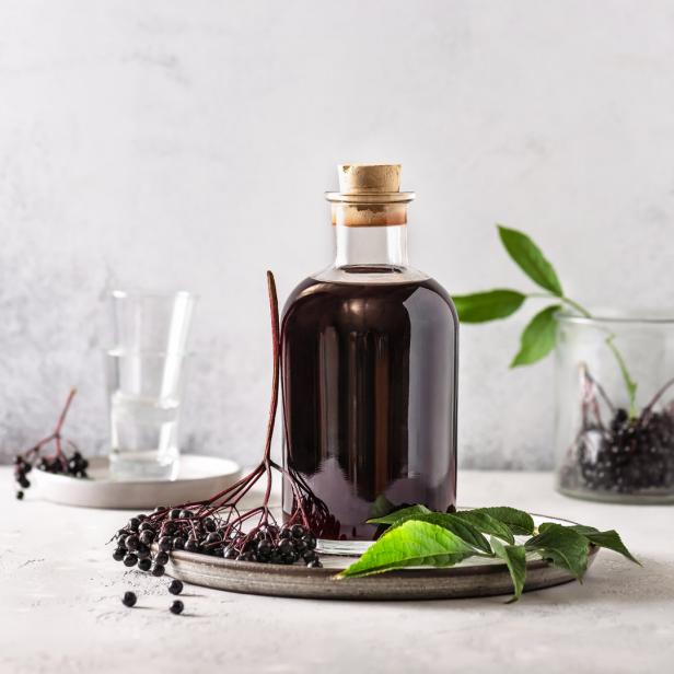 Eine Flasche Holundersaft steht auf einem Teller mit frischen Holunderbeeren.