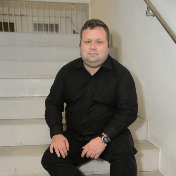 Ein Mann in schwarzem Hemd und Hose sitzt auf einer Treppe.