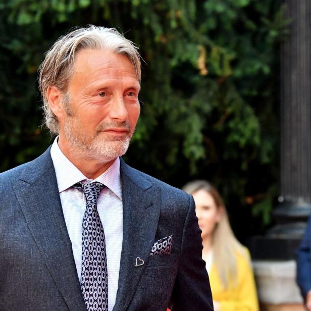 Mads Mikkelsen in einem grauen Anzug mit gemusterter Krawatte.