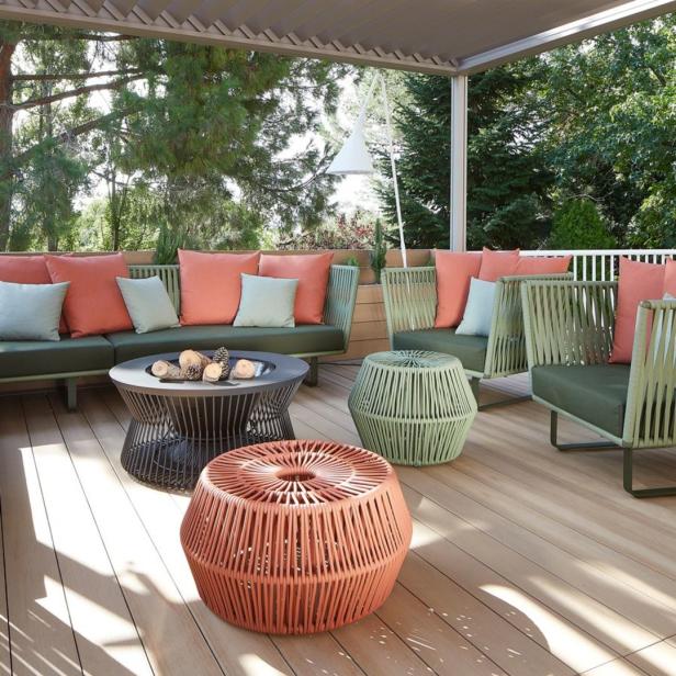 Eine Terrasse mit grünen Sofas, korallenroten Kissen und geflochtenen Hockern.