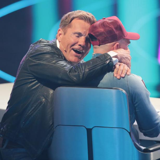 Dieter Bohlen umarmt einen anderen Mann auf einem Stuhl.