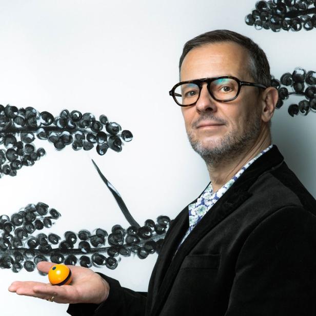 Ein Mann mit Brille hält einen kleinen orangefarbenen Ball in seinen Händen.
