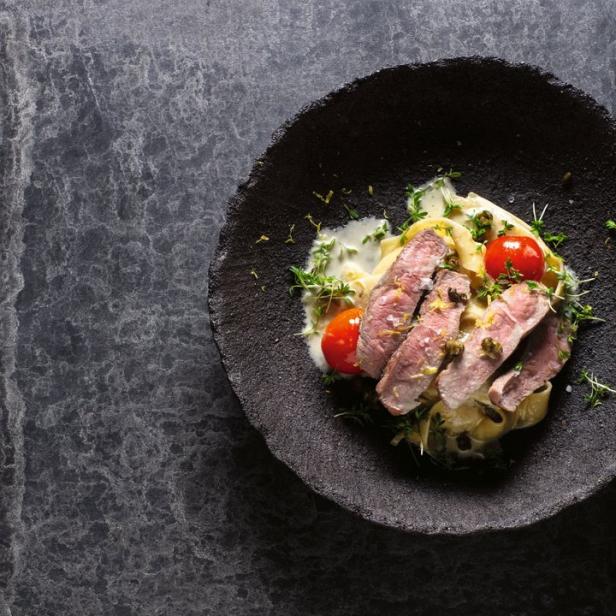 Ein Teller mit geschnittenem Steak, Pasta und Cherrytomaten auf dunklem Hintergrund.