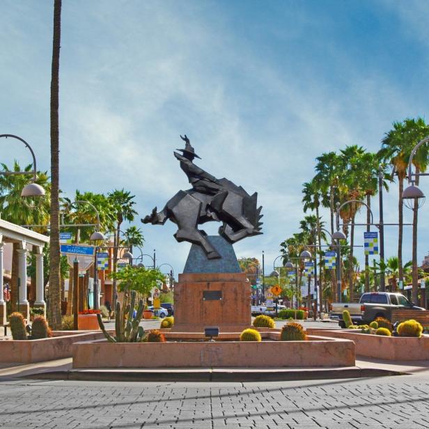 Eine Statue eines reitenden Cowboys in Scottsdale, Arizona, umgeben von Palmen und Kakteen.
