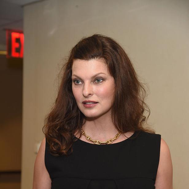 Linda Evangelista trägt ein schwarzes Kleid und eine goldene Halskette.