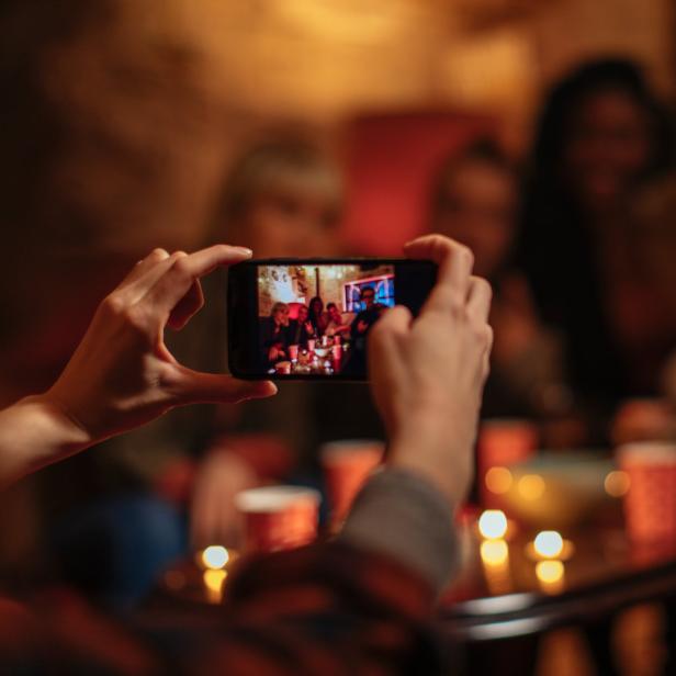 Eine Person fotografiert mit dem Handy eine Gruppe von Freunden auf einer Party.