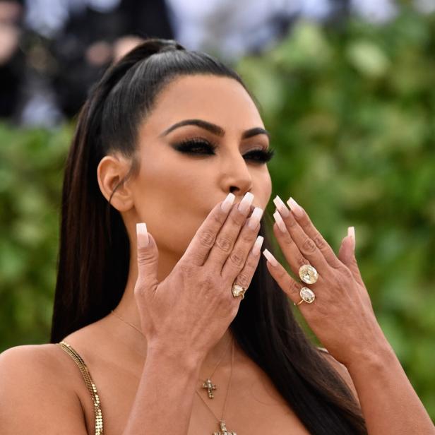 Kim Kardashian in einem goldenen Kleid mit Kreuzketten und großen Ringen, die einen Kussmund andeutet.