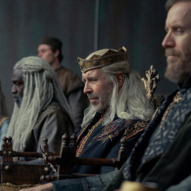 König Viserys Targaryen sitzt mit anderen Würdenträgern auf einem Thron.