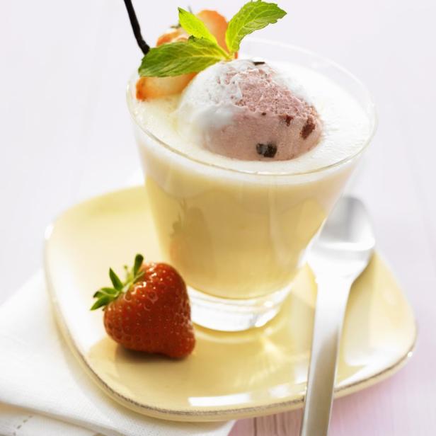 Ein Glas Dessert mit Vanillepudding, Erdbeeren, Minze und einer Kugel Eiscreme.