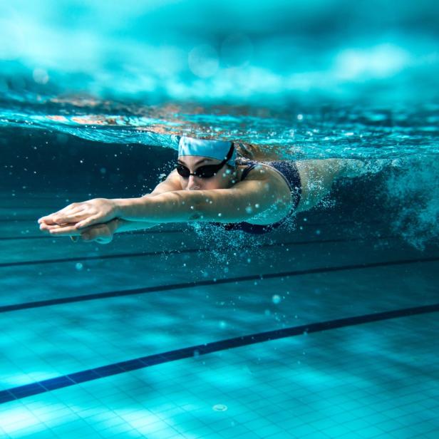 Eine Schwimmerin mit Badekappe und Schwimmbrille unter Wasser im Schwimmbad.