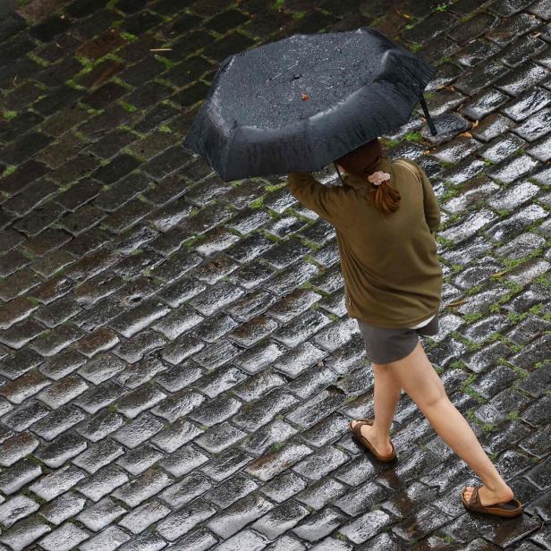 Eine Person geht mit einem Regenschirm über nasses Kopfsteinpflaster.