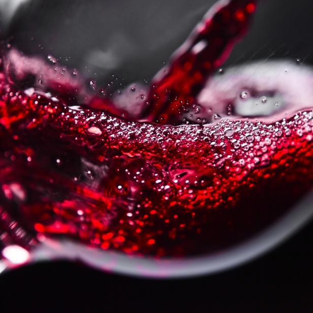 Rotwein wird in ein Glas gegossen, wobei sich viele kleine Bläschen bilden.