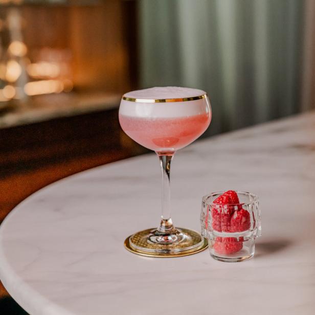Ein rosa Cocktail mit Schaum und Himbeeren auf einem Marmortisch.