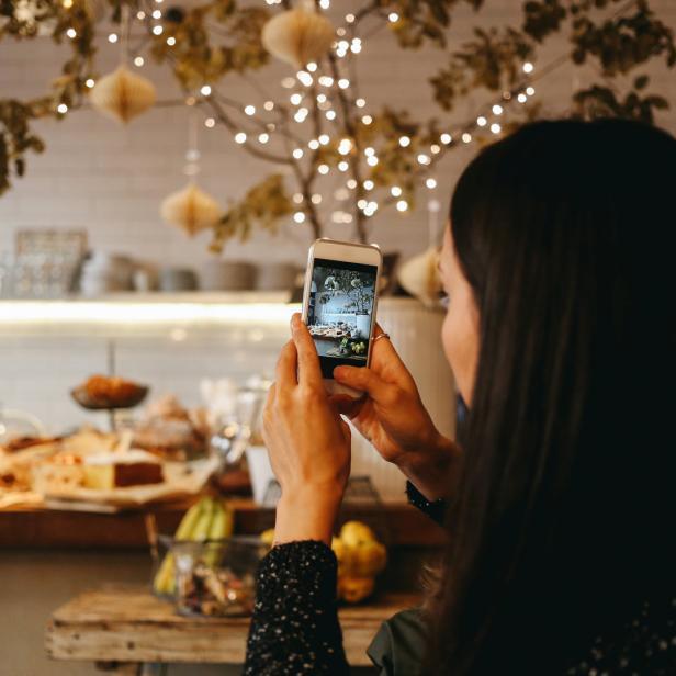Eine Frau fotografiert mit ihrem Smartphone eine Theke mit Speisen in einem Café.