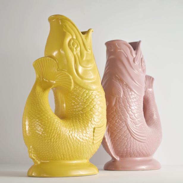 Zwei dekorative Vasen in Fischform, eine gelb und eine rosa, stehen nebeneinander.