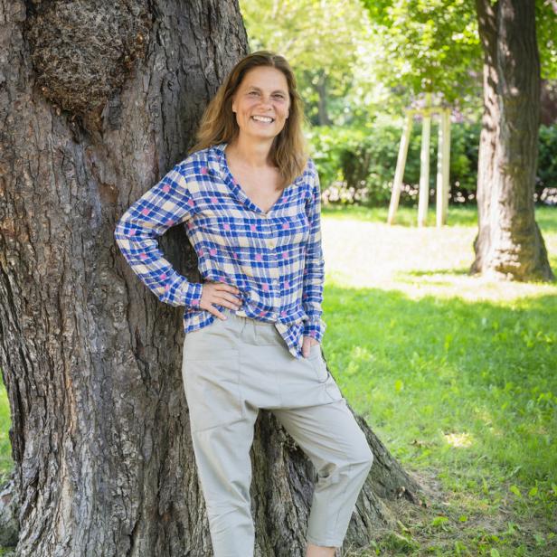 Eine Frau lehnt an einem Baum im Park.