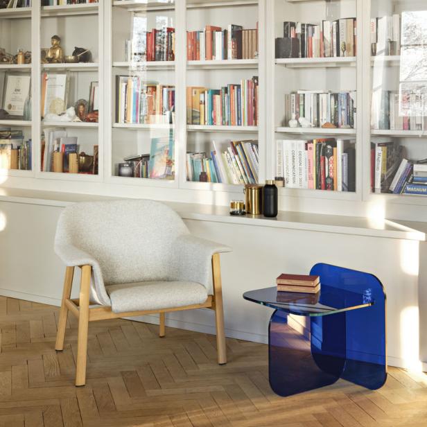 Ein Sessel und ein blauer Tisch stehen vor einem Bücherregal.