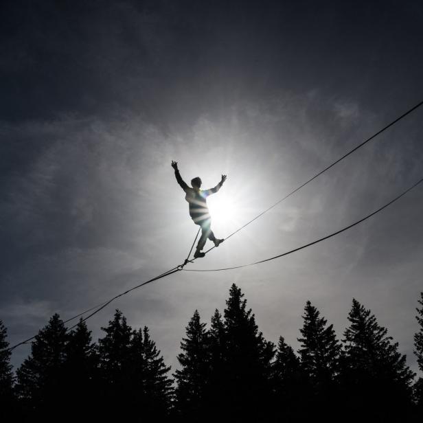 Eine Person balanciert auf einer Slackline vor dem Hintergrund der Sonne und einiger Bäume.