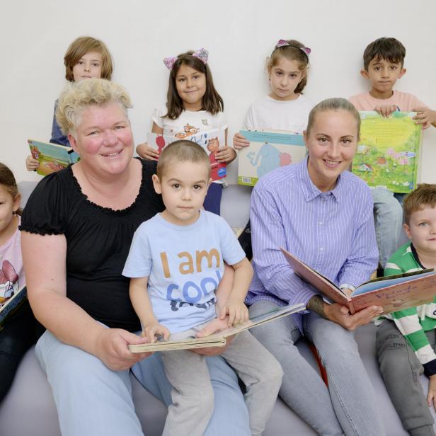 Eine Gruppe von Kindern und zwei Erzieherinnen sitzen zusammen und lesen Bücher.