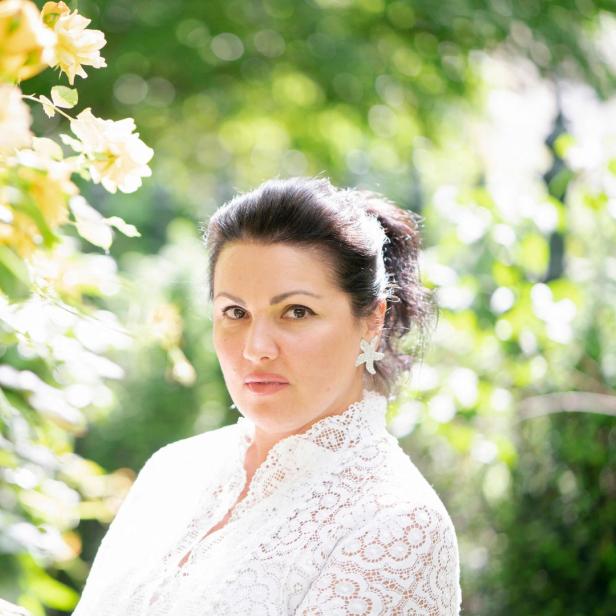 Eine Frau mit weißer Spitze steht vor gelben Rosen.