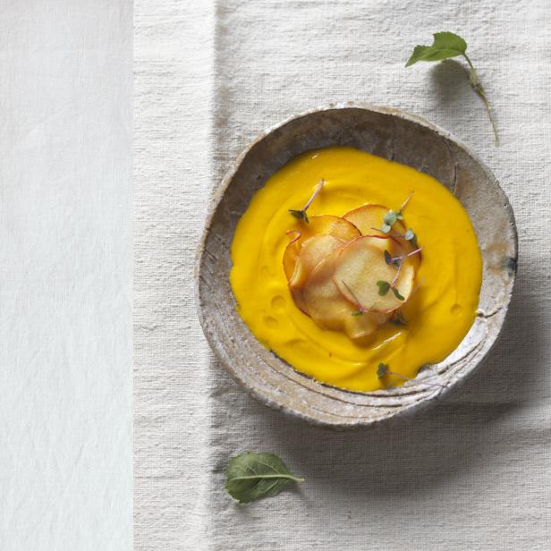 Eine Schüssel mit Kürbissuppe, garniert mit Apfelchips und Microgreens.