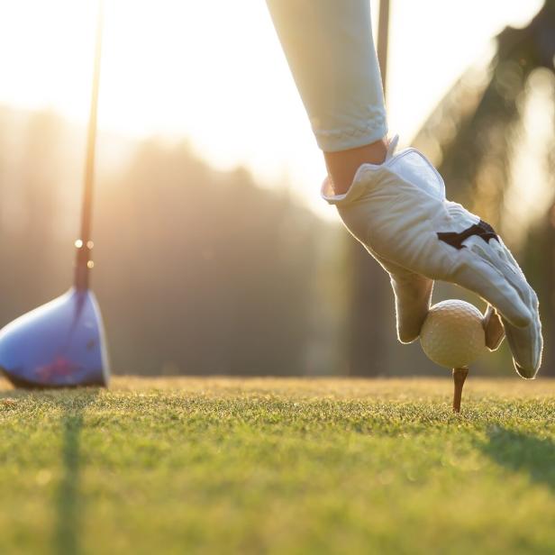 Eine Golferin platziert einen Golfball auf einem Holz-Tee auf dem Abschlag.