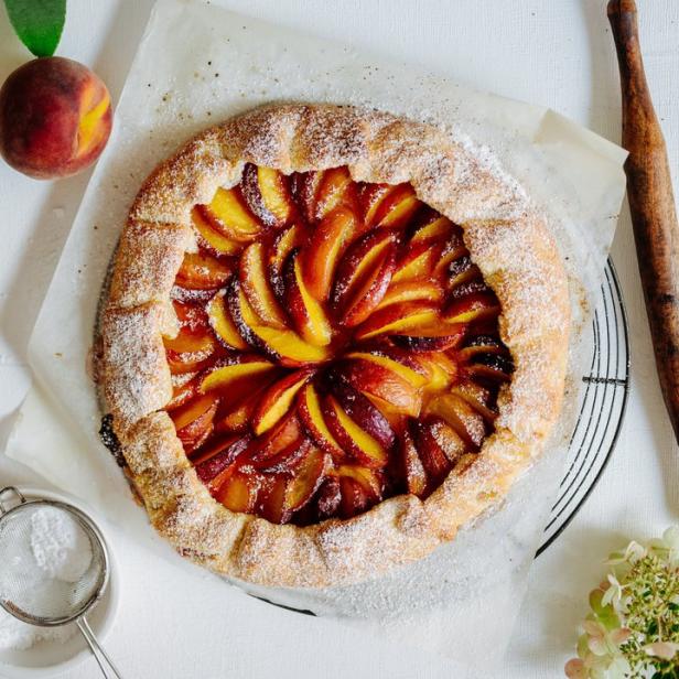 Ein Pfirsich-Galette, bestäubt mit Puderzucker, liegt auf einem Backpapier.