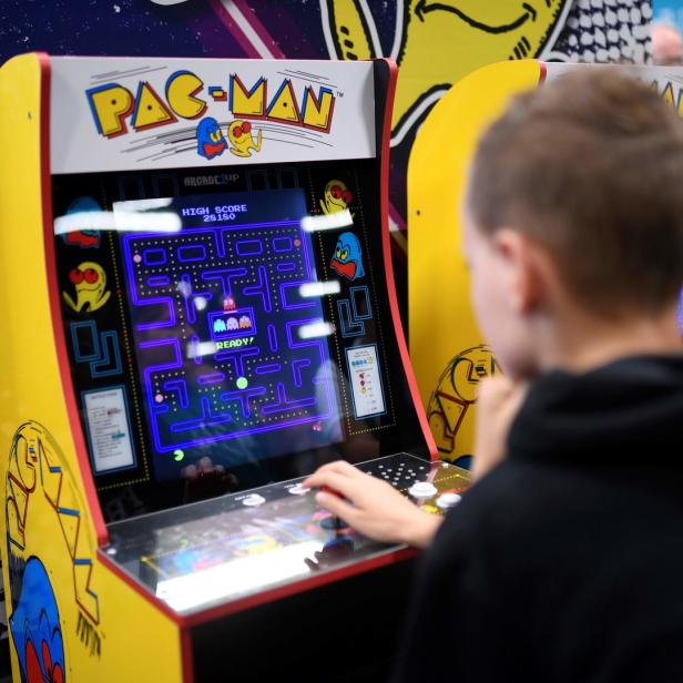 Ein Junge spielt an einem gelben Pac-Man-Spielautomaten.