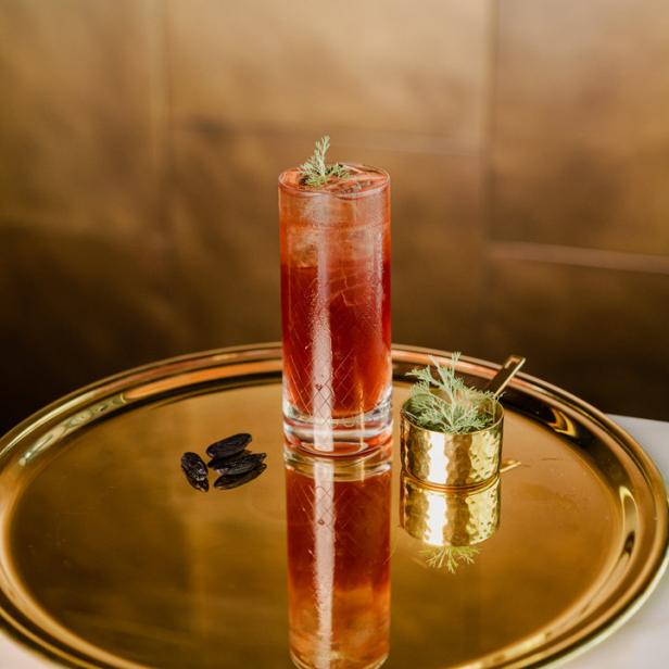 Ein Cocktail mit Eis und Kräutern auf einem goldenen Tablett mit Tonkabohnen.