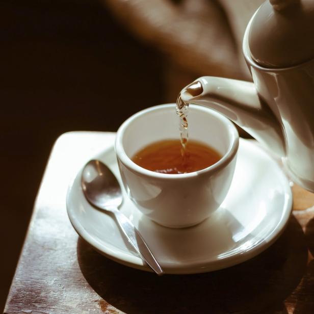 Tee wird aus einer weißen Kanne in eine Tasse gegossen.