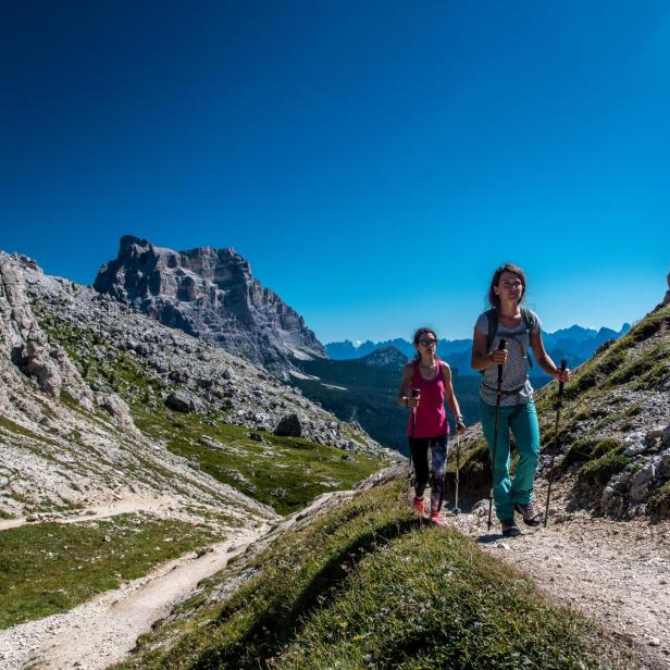 Zwei Frauen wandern mit Stöcken in den Dolomiten.