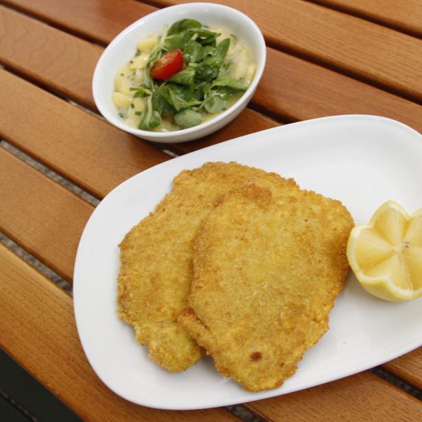 Ein Teller mit zwei Schnitzeln, einer Zitronenspalte und einem kleinen Salat.