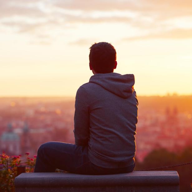 Ein Mann sitzt bei Sonnenaufgang auf einer Bank und blickt in die Ferne.