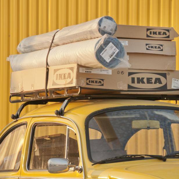 Ein gelber VW Käfer mit IKEA-Paketen und Teppichen auf dem Dachgepäckträger.