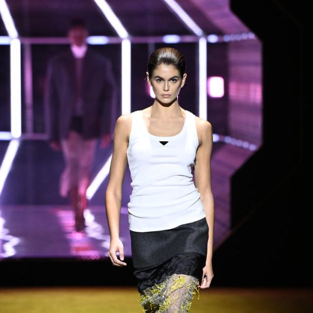Kaia Gerber läuft in einem weißen Tanktop und einem Rock mit gelben Akzenten über einen Laufsteg.