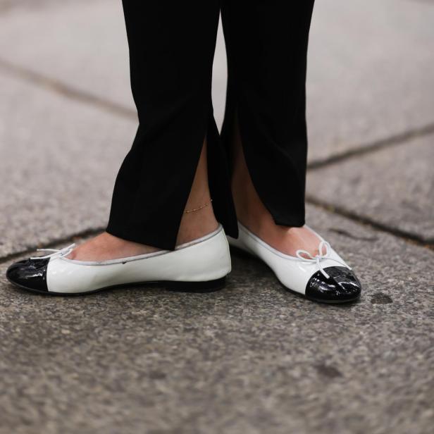 Nahaufnahme von schwarzen Hosen mit Schlitz und weißen Ballerinas mit schwarzer Spitze.