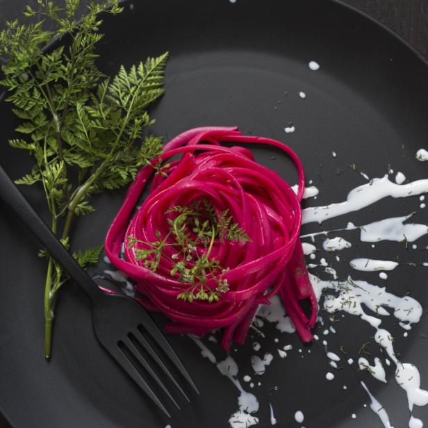 Ein Teller mit roter Pasta, garniert mit Dill und einer weißen Soße.