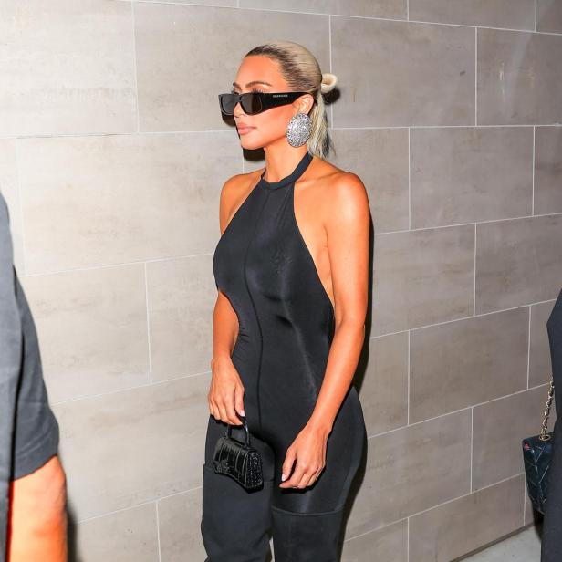 Kim Kardashian trägt einen schwarzen Overall, übergroße Ohrringe und eine „Balenciaga“-Sonnenbrille.