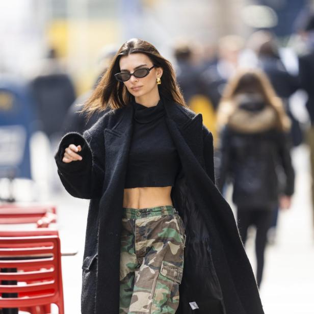 Emily Ratajkowski trägt eine schwarze Jacke, ein bauchfreies Oberteil und eine Camouflage-Hose.