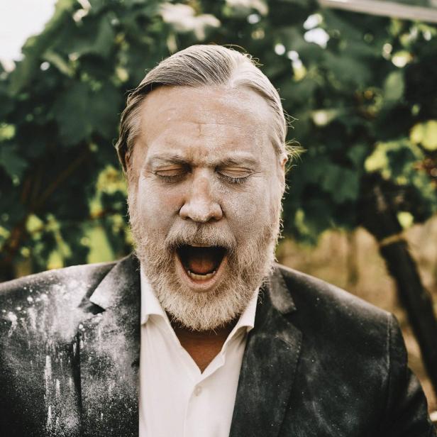 Ein Mann mit Bart und Anzug, bedeckt mit Puder, schreit vor einem Weinstock.