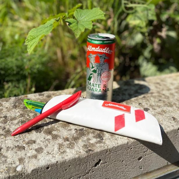 Eine Dose Almdudler Mate, ein Mäppchen und ein Stift liegen auf einer Mauer.