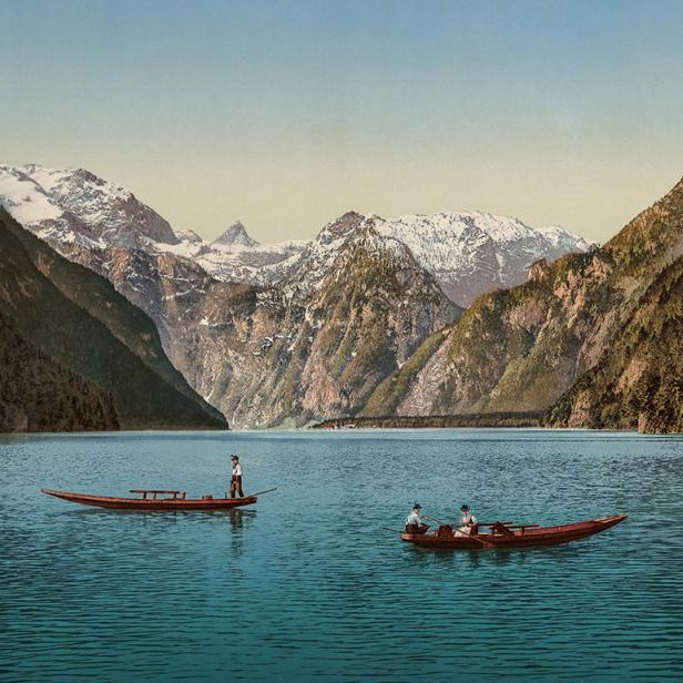 Zwei Boote fahren auf einem See vor einer Bergkulisse mit schneebedeckten Gipfeln.